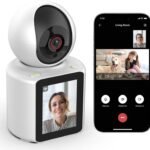 Dispositivo de vigilancia doméstica blanco con cámara esférica y pantalla frontal junto a un smartphone que muestra la app en videollamada con una mujer y una niña con su perro, SHIWOJIA Cámara WiFi interior, cámara monitor anciano/niño con llamada con un botón, audio de 2 vías, rotación 360°, visión nocturna, detección de movimiento, ideal para monitorizar niños, ancianos y mascotas y controlar la cámara remotamente desde la aplicación.