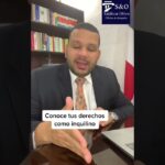 Hombre de traje sentado en un despacho con estantería de libros, bandera y logo de oficina de abogados, hablando frente a la cámara y ofreciendo consejos legales para inquilinos, destacando Negociar con okupas antes de denunciar al propietario como alternativa y guía práctica.