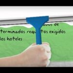 Mano que sostiene un limpiador de cristal azul limpiando un cartel verde con texto parcial sobre requisitos a los hoteles, imagen clara y accesible que acompaña la frase Parlament solicita agilizar desalojo de okupas en hoteles.