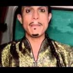 Hombre de 78 años expulsa okupas de su casa de forma ingeniosa, retrato de un hombre con maquillaje oscuro y chaqueta dorada sentado en el interior de un vehículo.