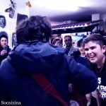 Grupo de personas en interior con músico tocando guitarra y joven sonriente, okupa vive en casas de 4.500€ en Madrid sin pagar alquiler