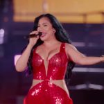 Cantante en un concierto vestida con un llamativo traje rojo de lentejuelas, sosteniendo un micrófono y gesticulando con un brazo extendido sobre un escenario iluminado mientras proyecta energía y emoción en su actuación, El drama invisible en el fútbol un año tras la dana.